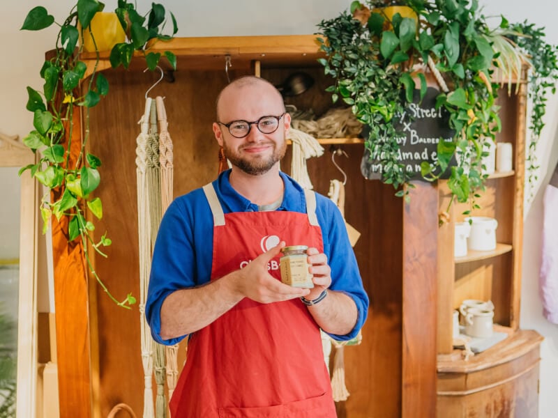 A man wearing an apron holding a handmade candle