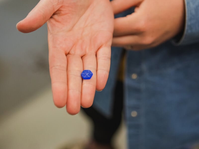 Close up of a hand holding a small blue wax casting of a gemstone shape