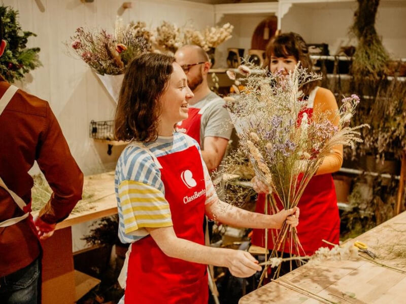 Three people smiling as they admire the dried flower bouquets they have made