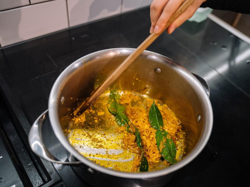 Using a wooden spoon to bloom spices in a metal saucepan