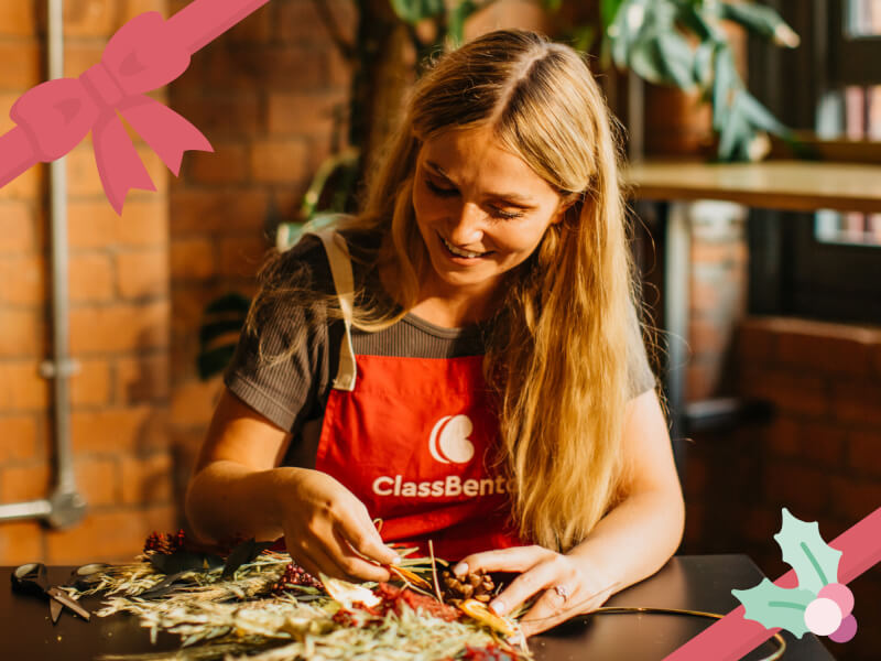 A woman smiles as she works on a dried flower Christmas wreath