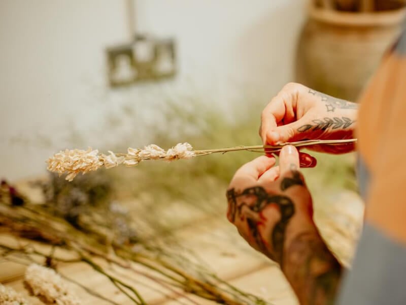 Close up of a man with tattooed hands arranging dried flowers
