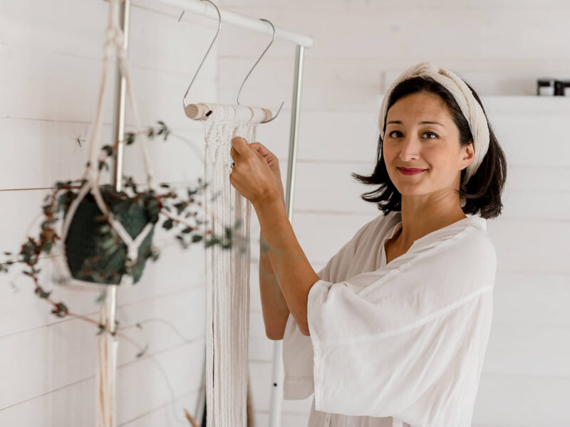 Macrame teacher and business educator, Isabella Strambio, making a macrame wallhanging from white cord and smiling