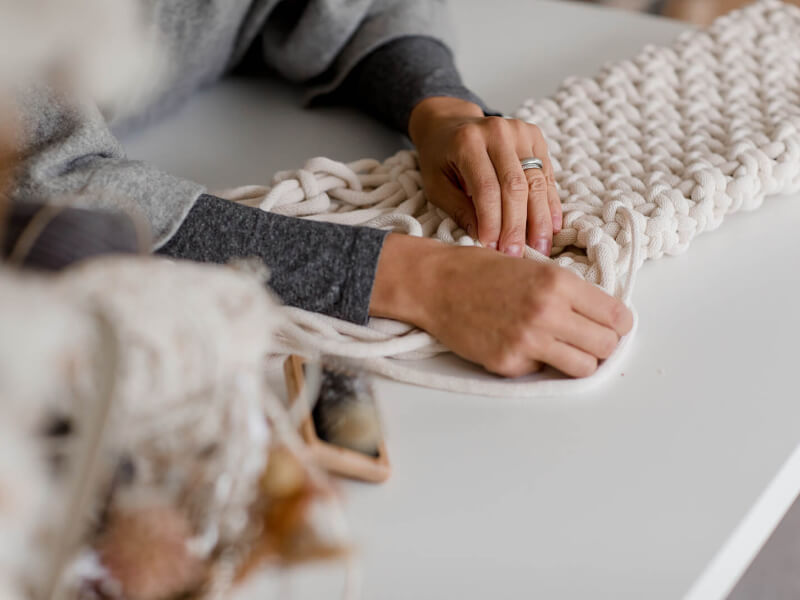 A close up of two hands working on a DIY macrame piece in cream cord