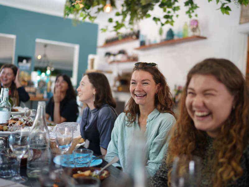 A group of people sit around a table at dinner, laughing and smiling