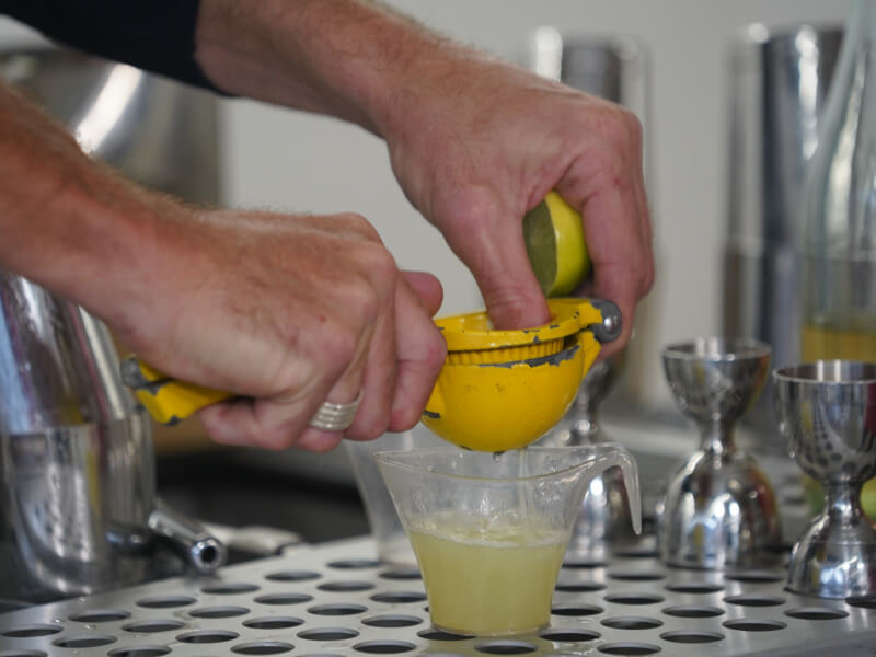 A close up shot of a pair of hands squeezes lemon juice into a small glass ready to make a cocktail