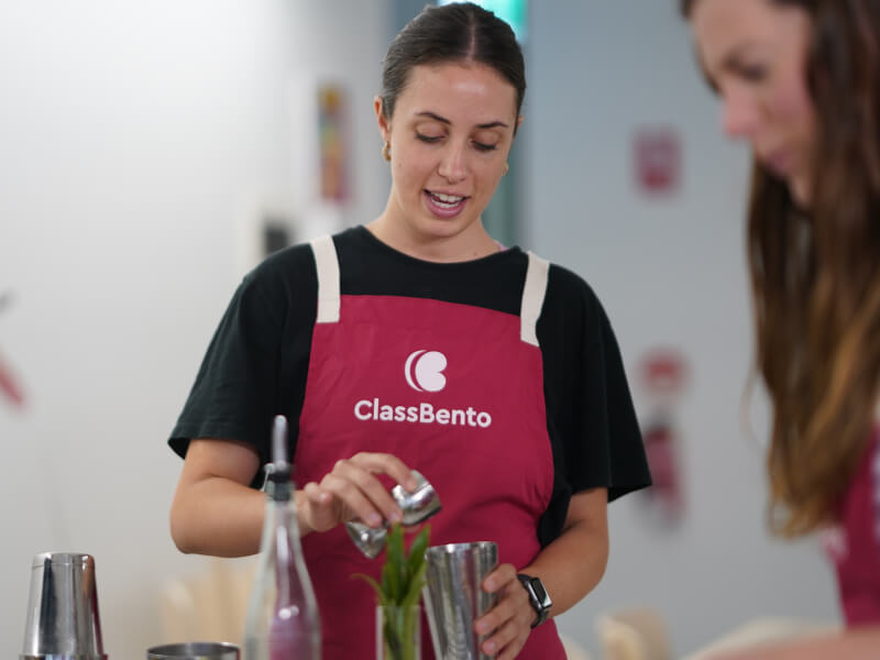 A woman wearing a pink apron making cocktail at a cocktail masterclass. 