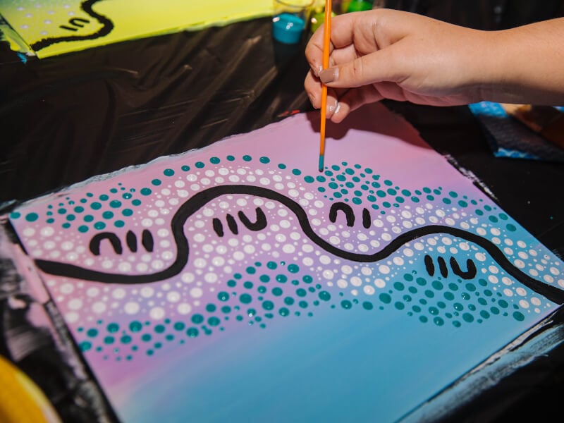 Abstract painting made up of black squiggles as well as white and turquoise dots being made with a paintbrush end