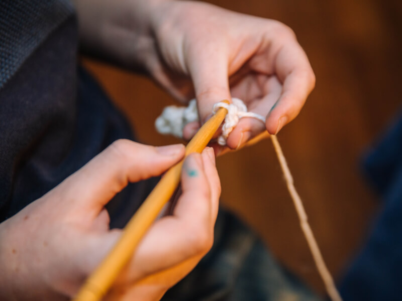 A close up of a person learning to crochet with a wooden crochet hook and cream yarn