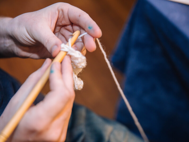 A close up shot of a person crocheting with a wooden crochet hook and white yarn