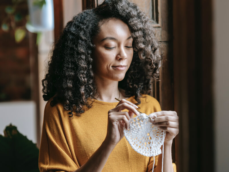 A woman is crocheting in the round using white yarn and a silver crochet hook