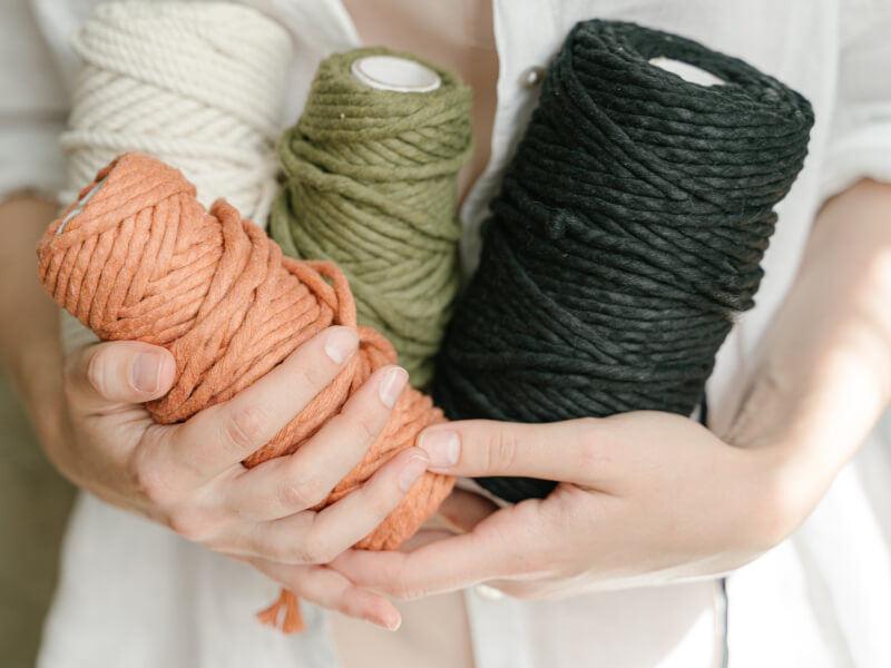A person is holding four balls of yarn in orange, white, grey and green