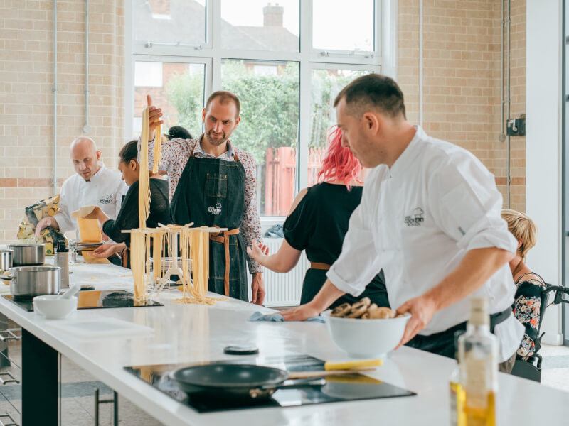 A man wearing chefs whites is teaching a group of people how to make fresh pasta