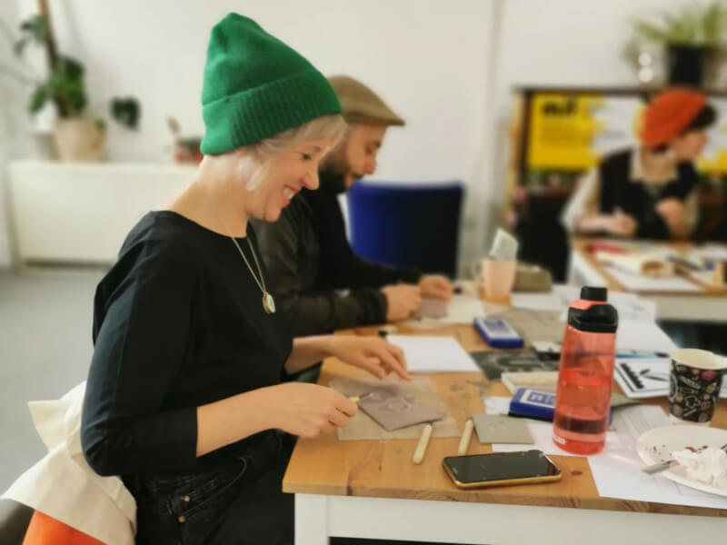 A group of people are sitting at a table, carving lino blocks ready to print