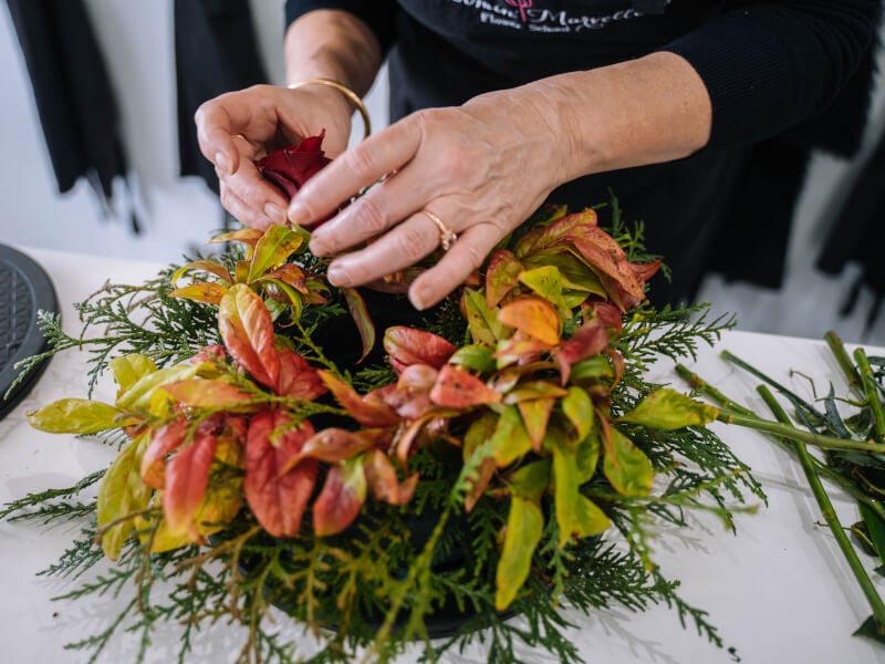 A person adds decorations to their festive arrangement in a wreath class.