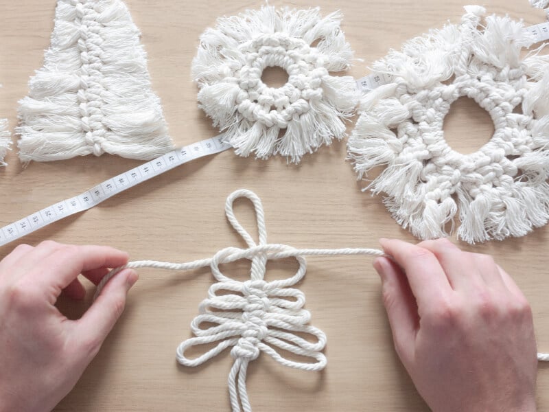 A close up of a person making a macrame Christmas decoration in white cord