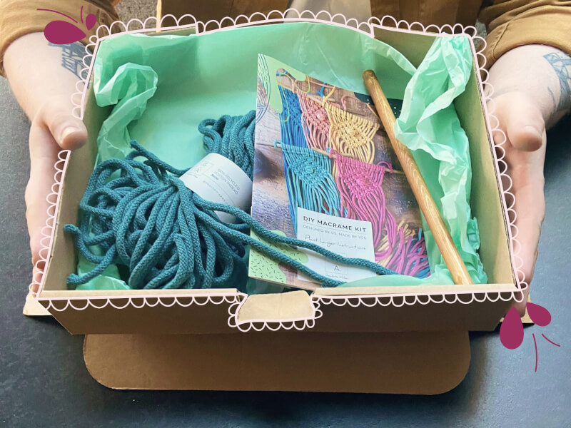 A DIY macrame craft box containing green tissue paper, blue coloured macrame cord and an instruction booklet