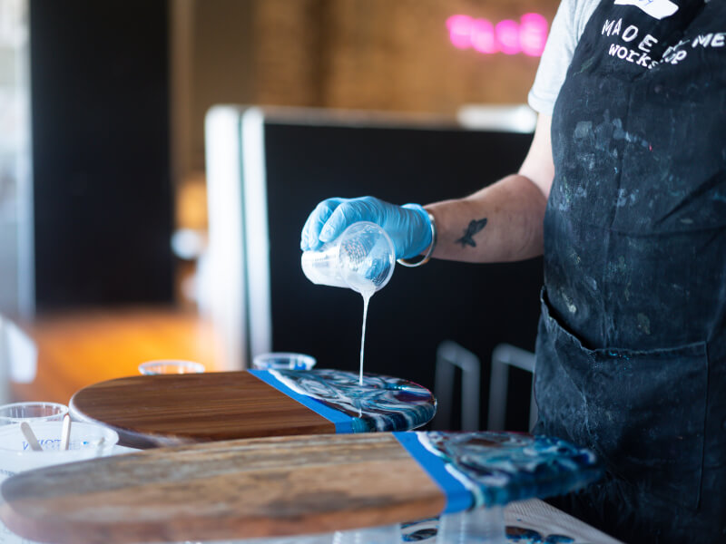 A person wearing apron pouring paint at a fluid art class.