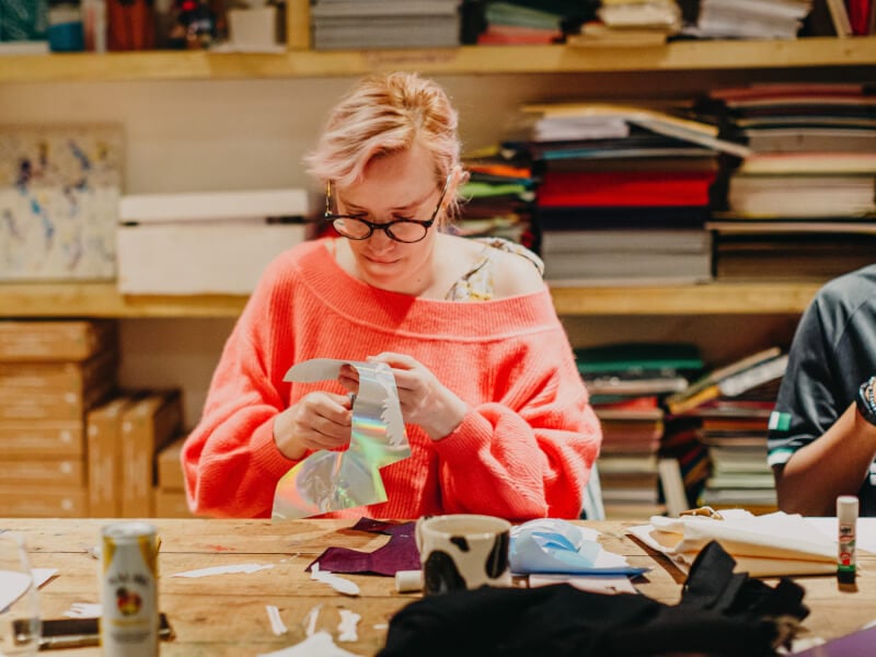 A person at a sewing class, cutting out holographic paper with scissors