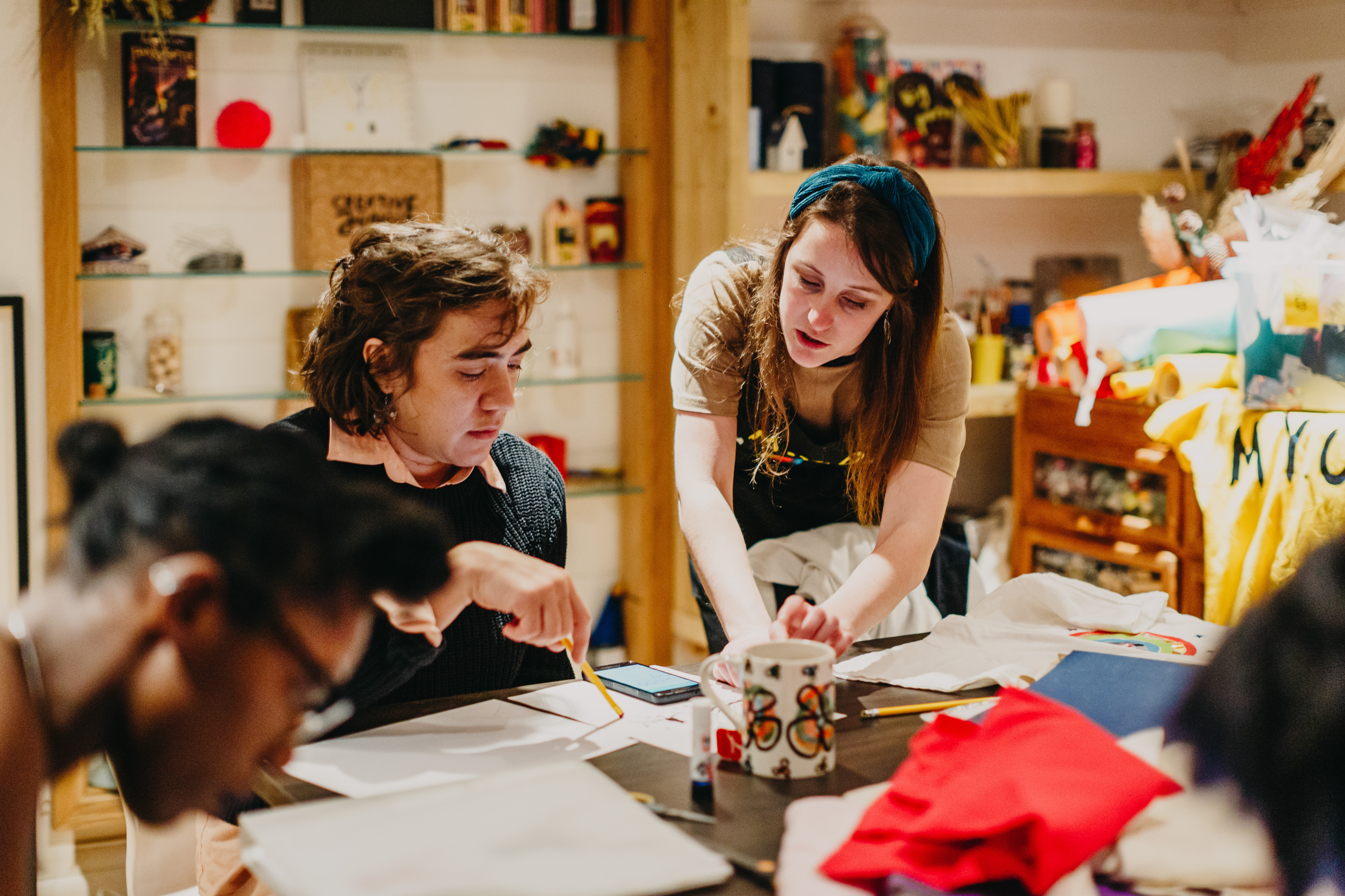 A teacher is talking to a student sitting at a table in a sewing workshop