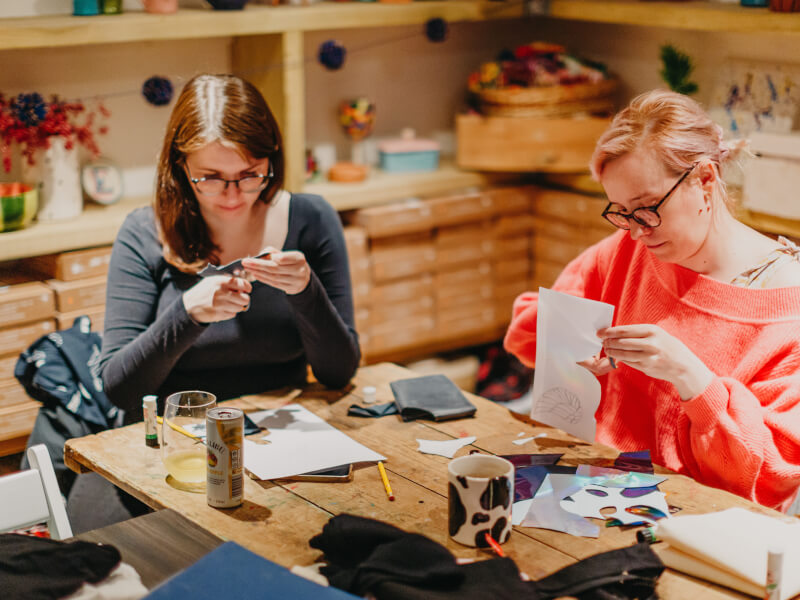 Two people sat at a table, cutting paper stencils with scissors