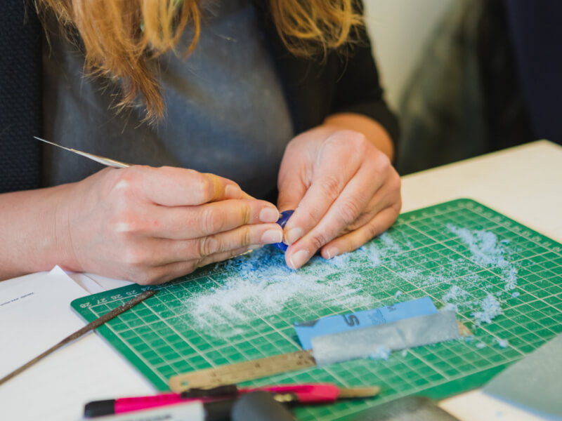 A close up of a person working on a blue wax mould to create handmade jewellery