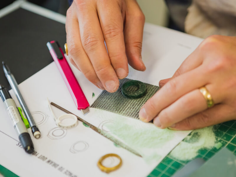 A close up of a person making a green wax mould for a silver ring at a jewellery making class