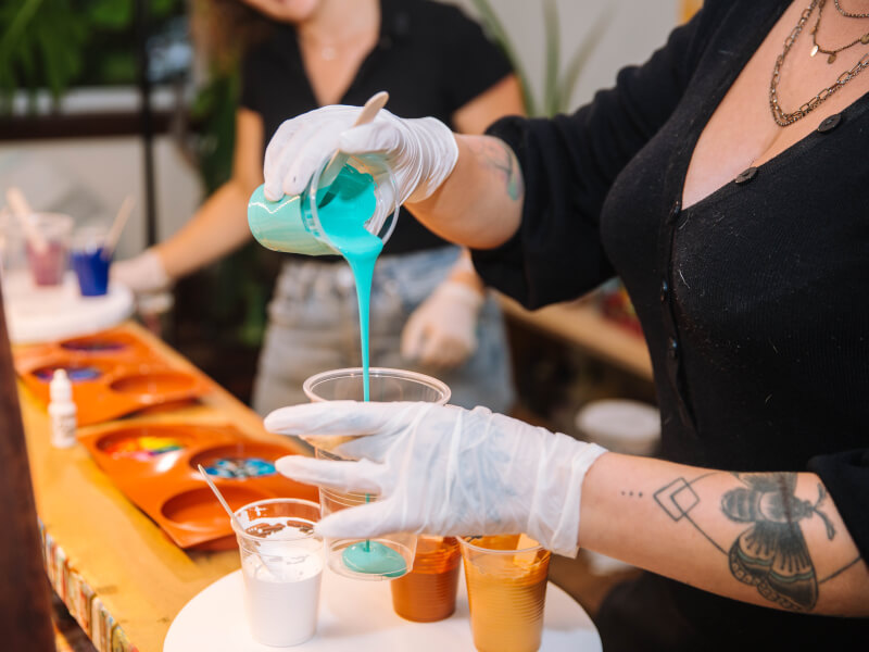 A person is adding aqua coloured paint to a cup at a paint pouring art class in Edinburgh