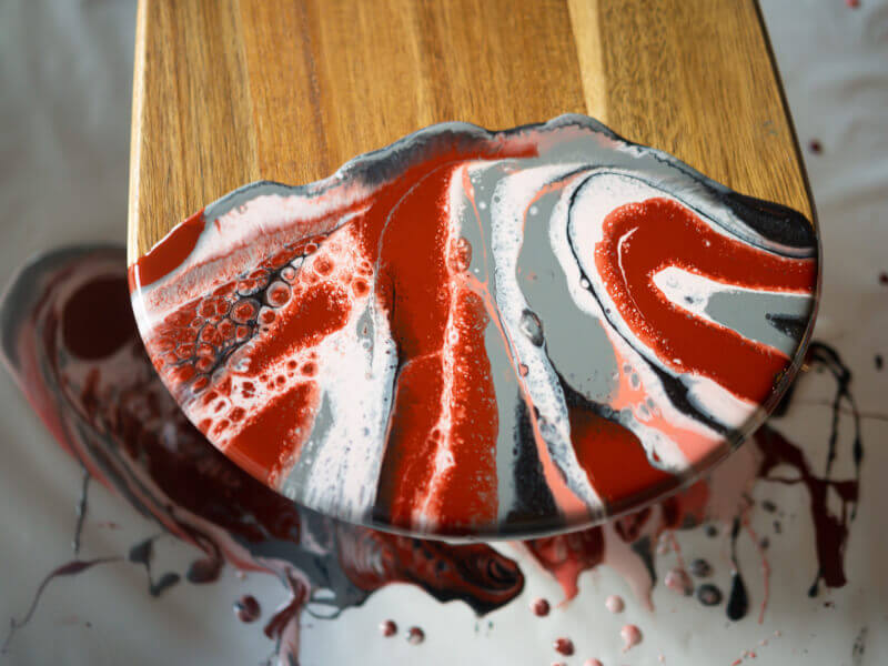 A picture of a finished chopping board decorated in red, grey and white paint using the paint pouring technique