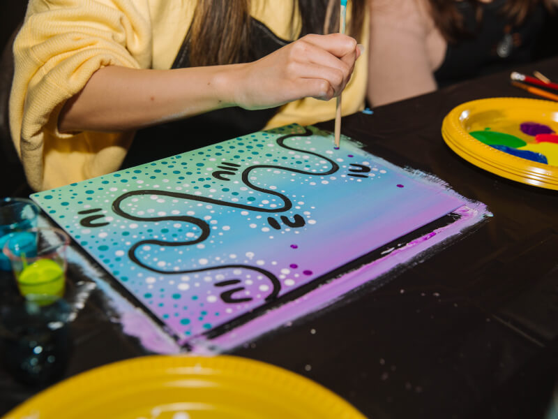 A person is painting an abstract picture using aqua, purple and black paint at an art class in Edinburgh