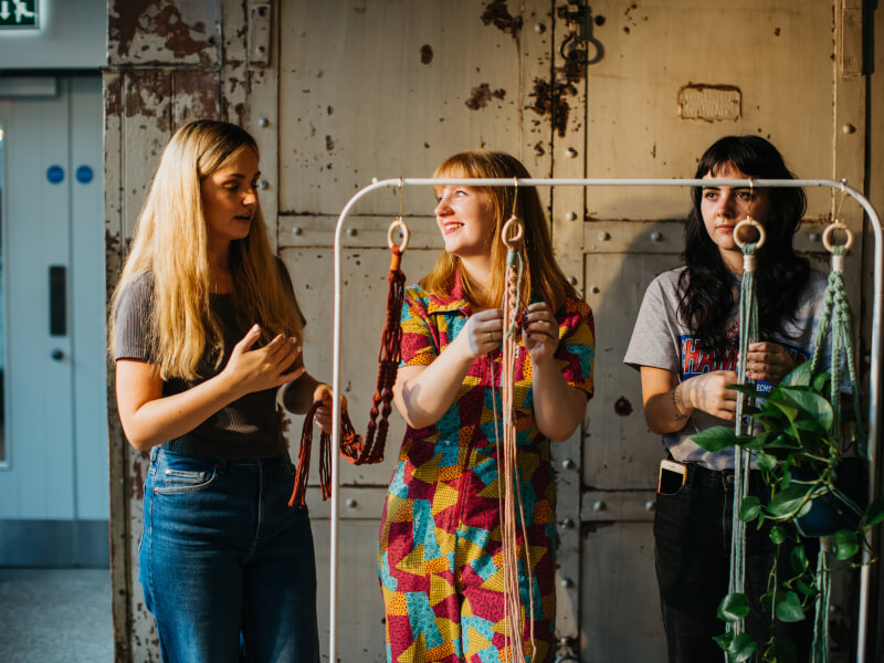 Three woman are learning macrame whilst standing up.