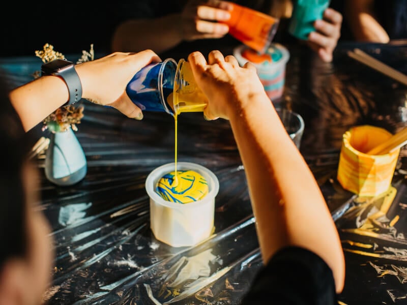 Someone pouring two brightly coloured resins to make a pot in a Manchester craft class.
