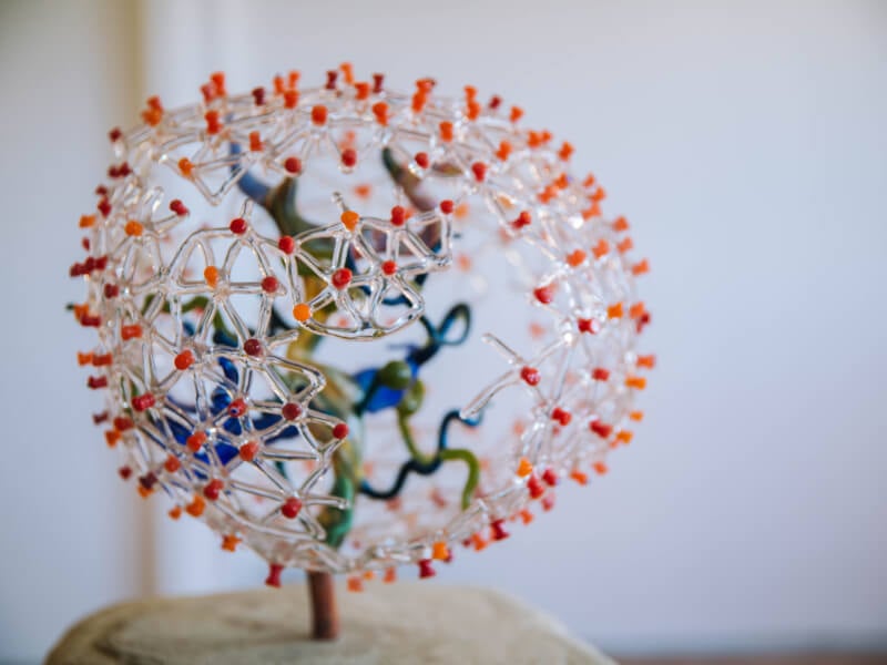 A piece of hand blown glass art with red and orange points and clear webs.