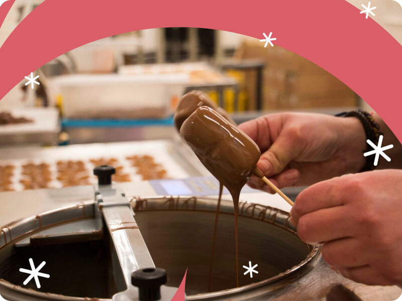 A person is holding sweets on sticks covered in melted chocolate over a bowl