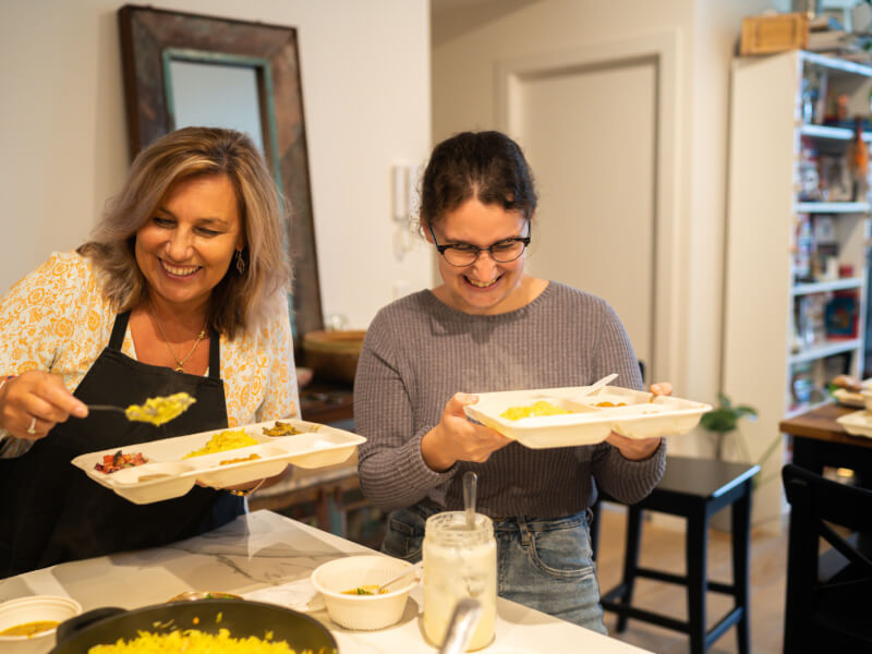 Two women smiling as they plate up food on sectioned trays