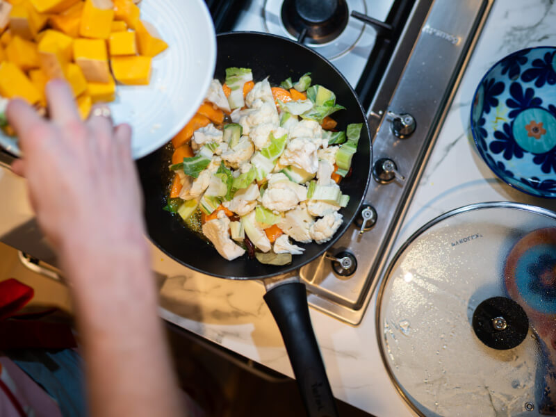 Someone adds butternut squash to a frying pan full of other vegetables.