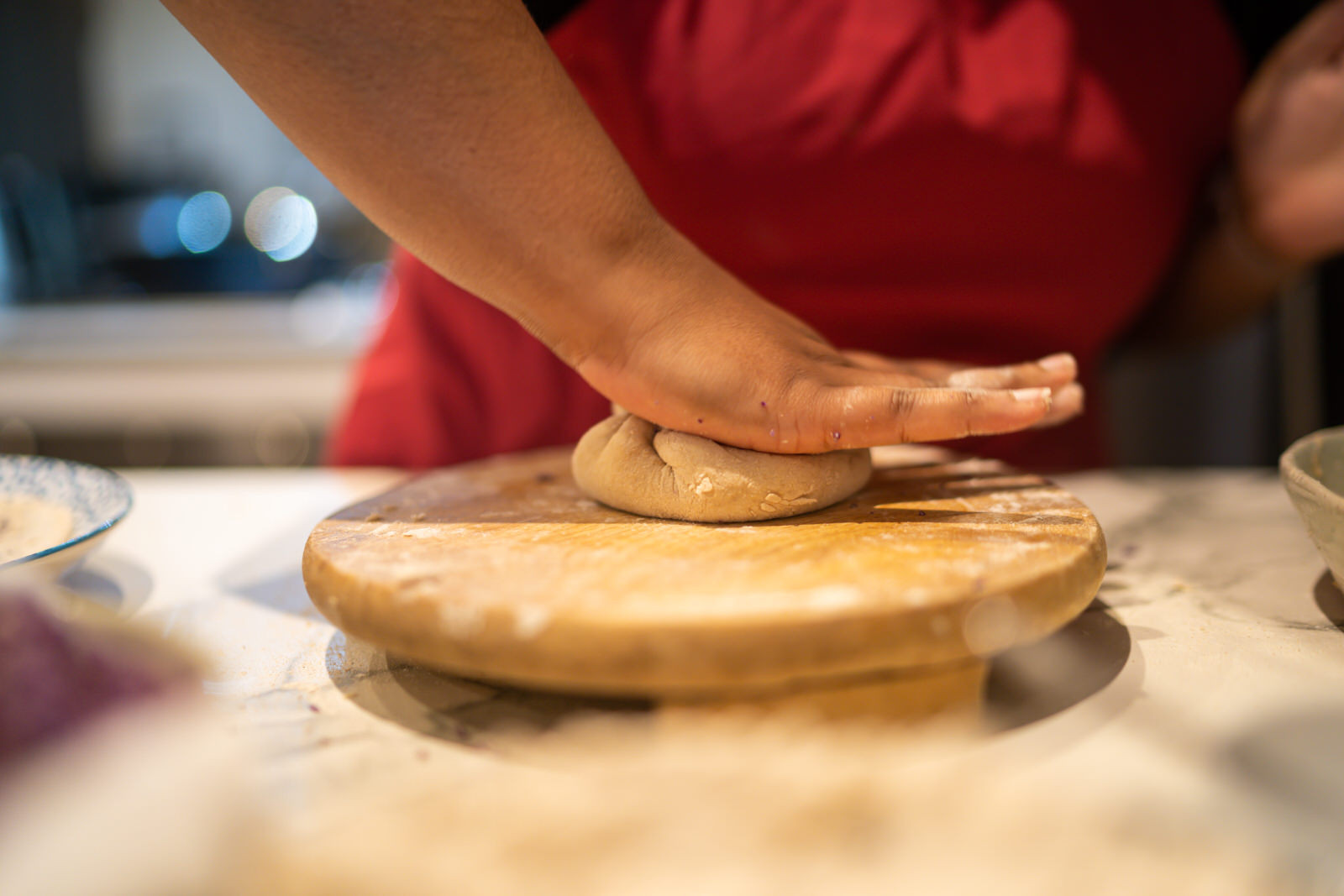 A person flattens a ball of dough on a wooden board.