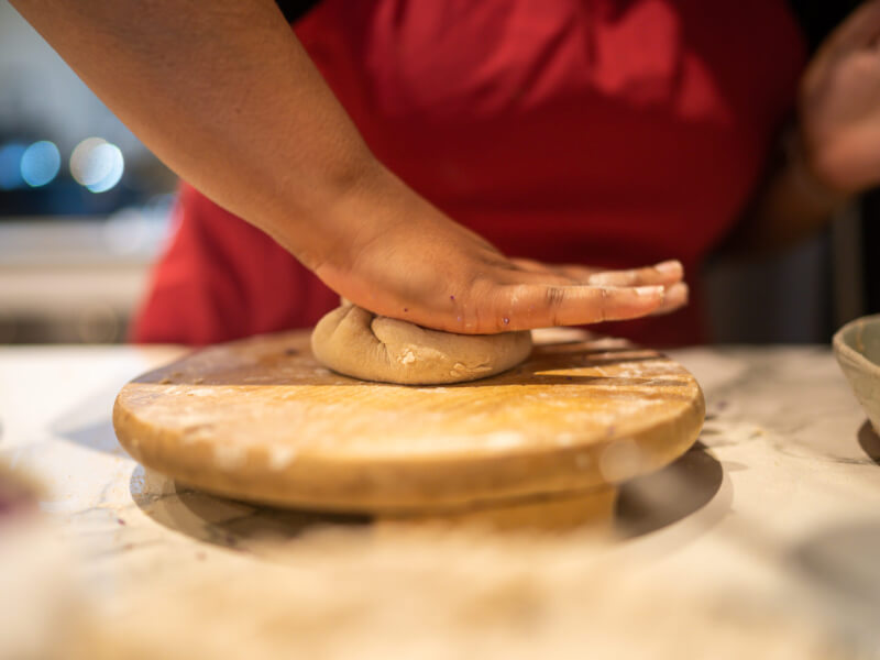 A closeup of a woman flattening dough at a cooking class.