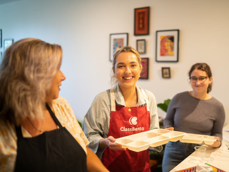 Woman smiling holding a Thali tray at an Indian cooking class.