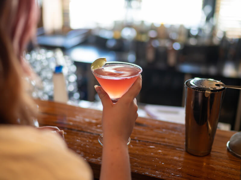 The back of a woman head as she hold a cocktail on a bar.