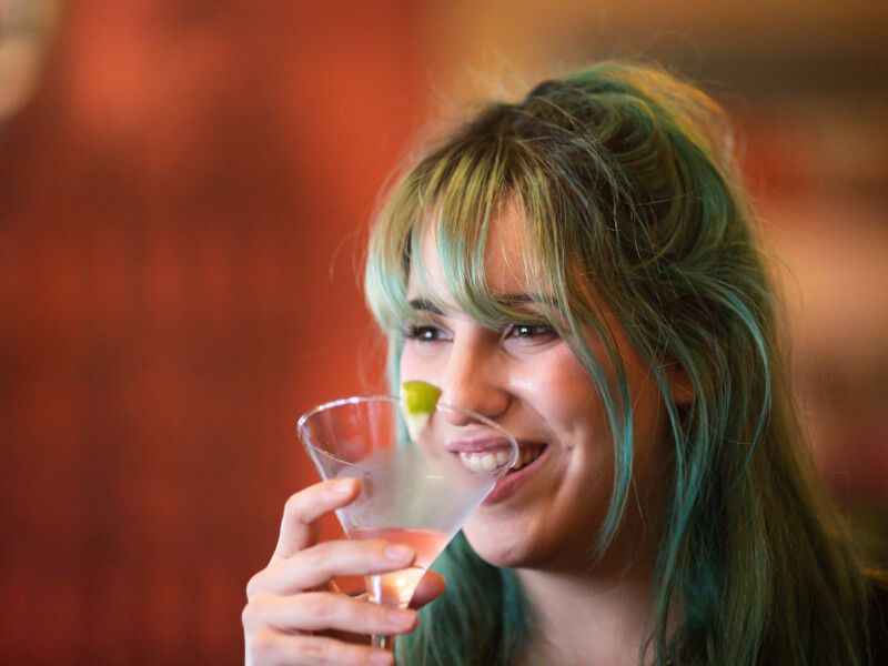 Woman smiling whilst sipping cocktail at a cocktail masterclass.