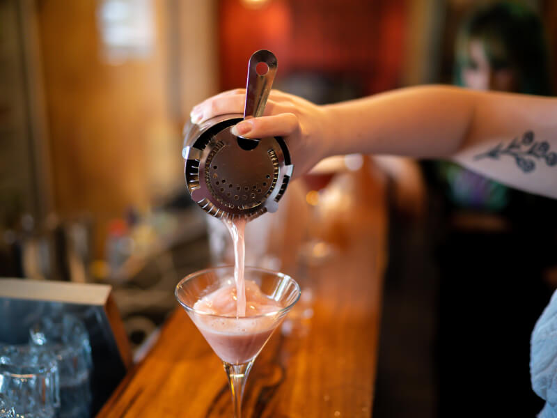Someone pours a pink summer cocktail into a glass from a shaker.