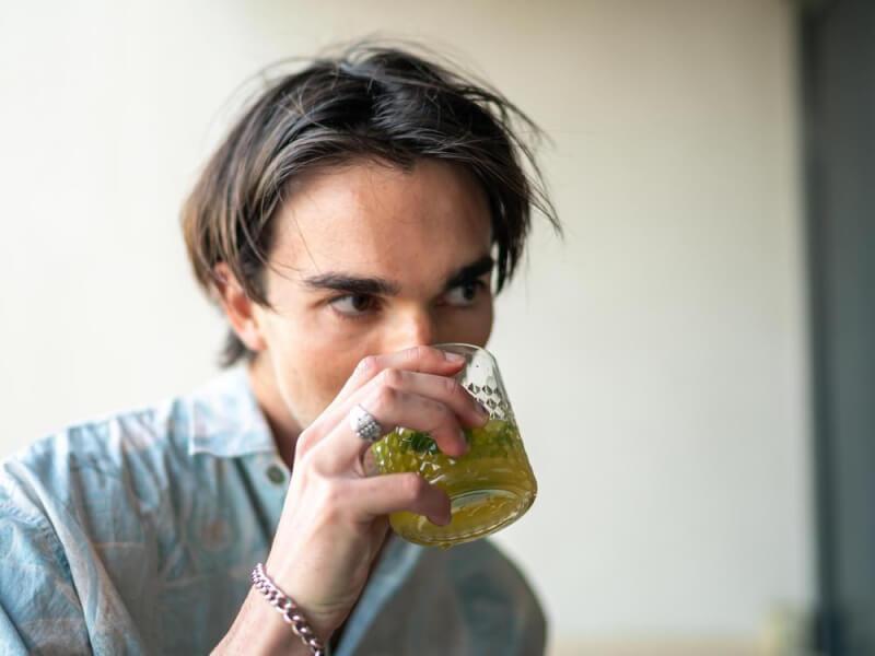 Close up of a man sipping a pale green cocktail from a rocks glass