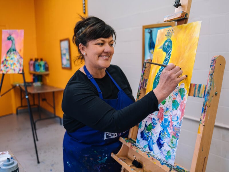 A woman learns how to paint a colourful peacock.