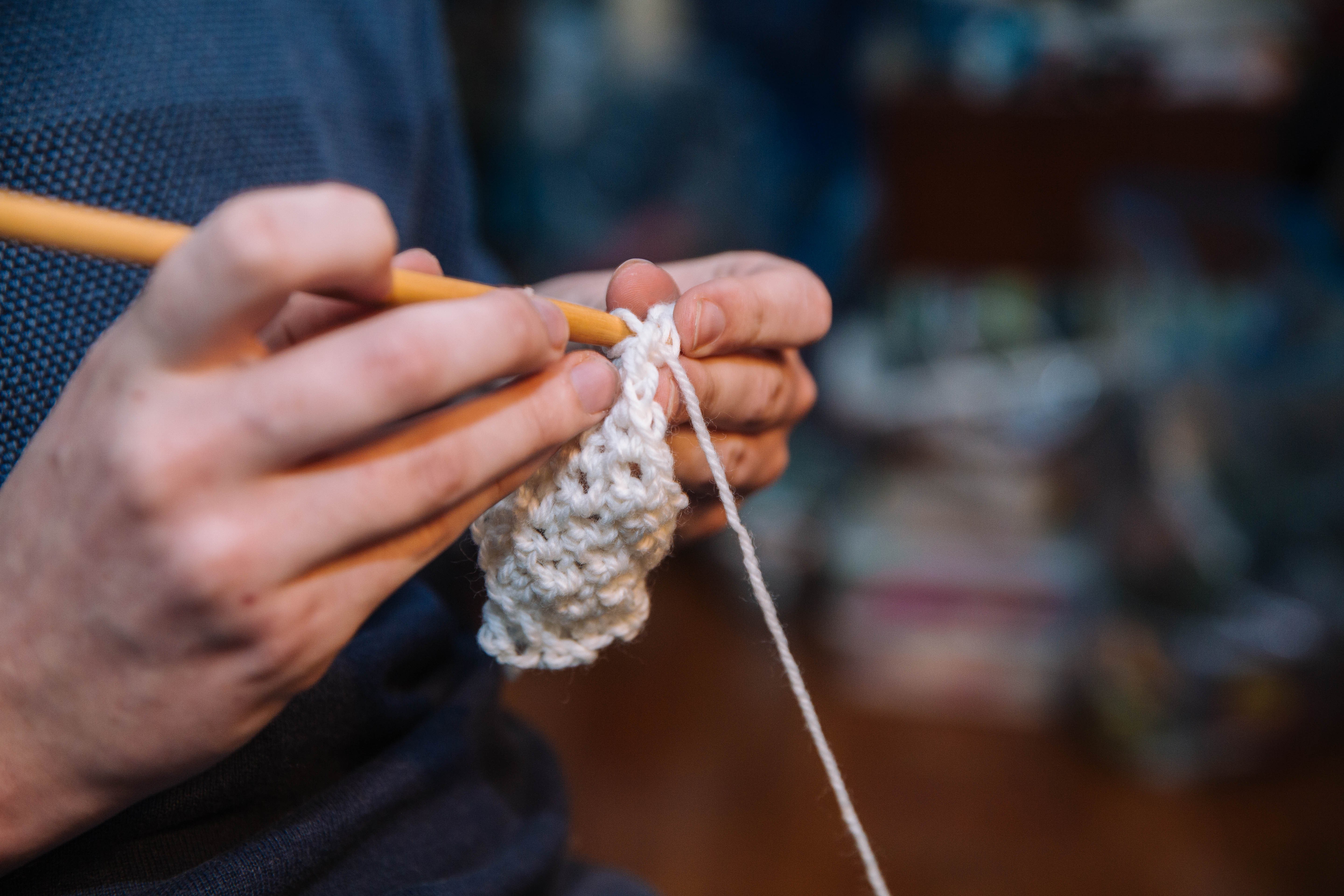A man uses a crochet hook to make a few lines of crochet stitches.