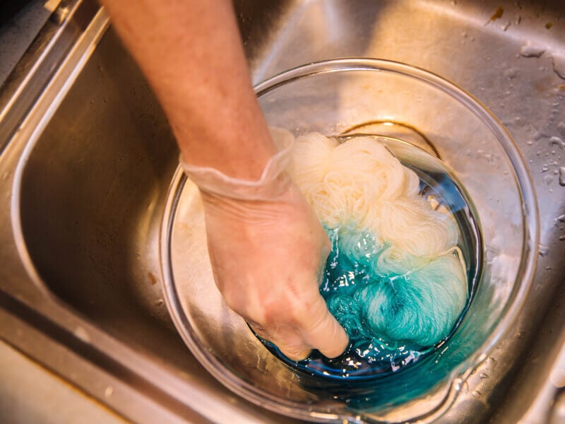 Close up of a person placing a dyed wool hank in a bowl of fixative.