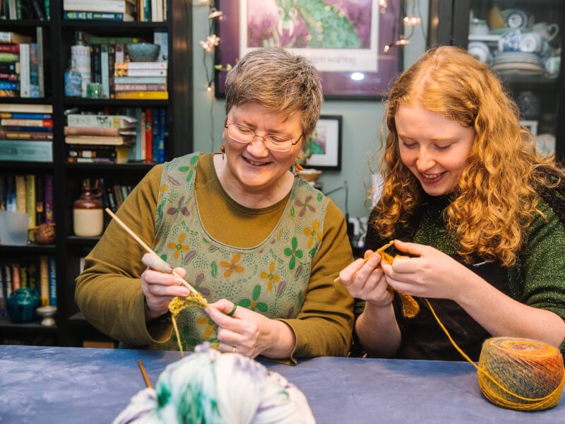 Two women crocheting at a craft class.