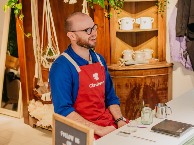 A man wearing a blue shirt is sitting at a table with candle making equipment in front of him