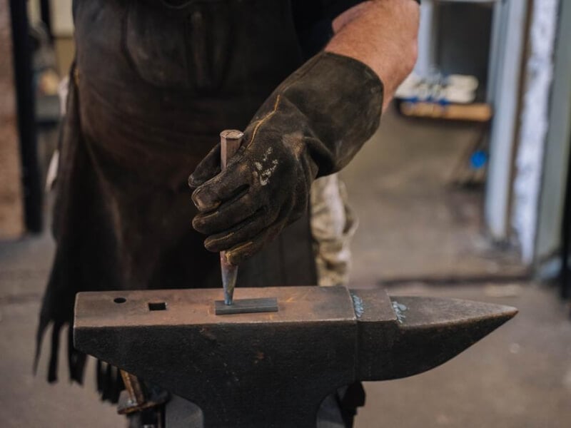 Close up of a hammer striking a piece of metal on a blacksmith's anvil