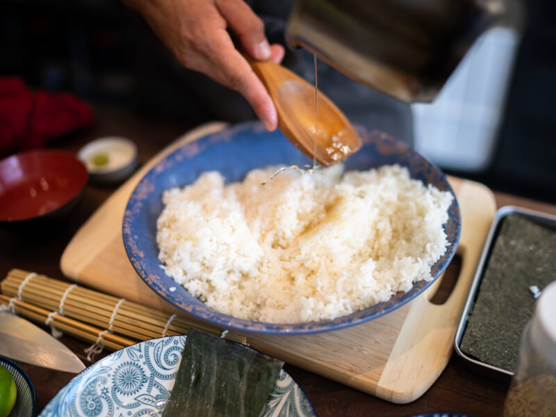 Close up of a wooden spoon serving white rice into a porcelain bowl